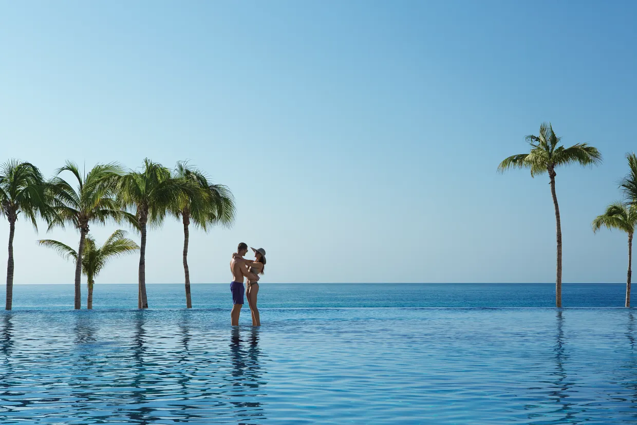 Couple at infinity pool overlooking the ocean — all-inclusive honeymoon resorts for Canadians